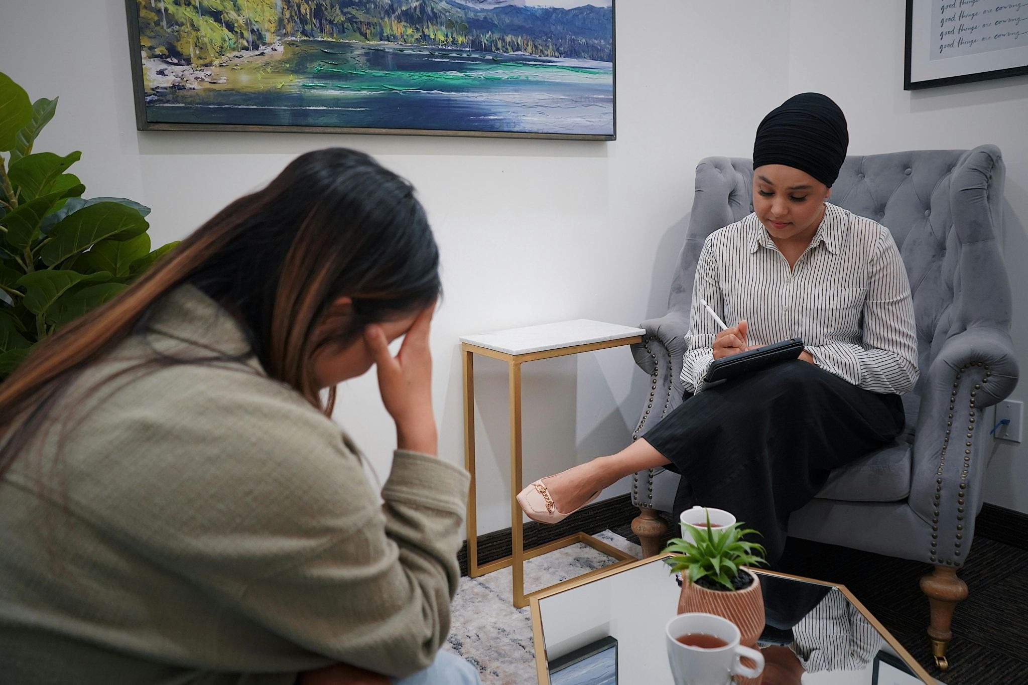 A picture of one person taking notes while the other person is talking with their head in hands